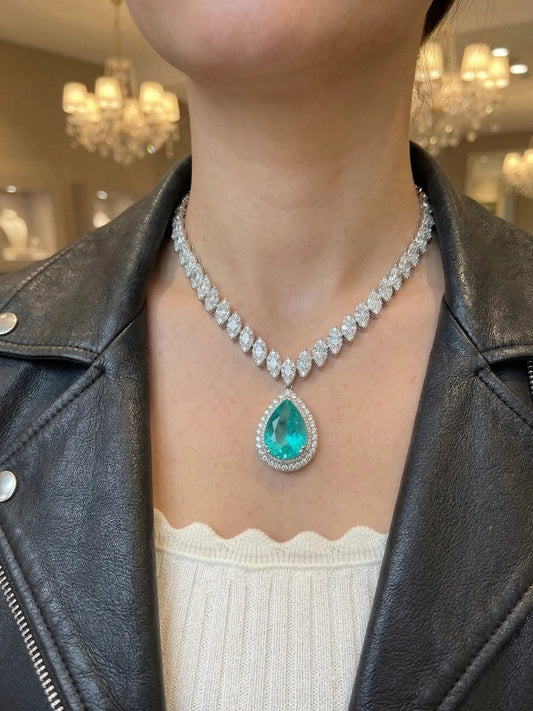 Person wearing a necklace with a green gemstone in a blurred indoor setting