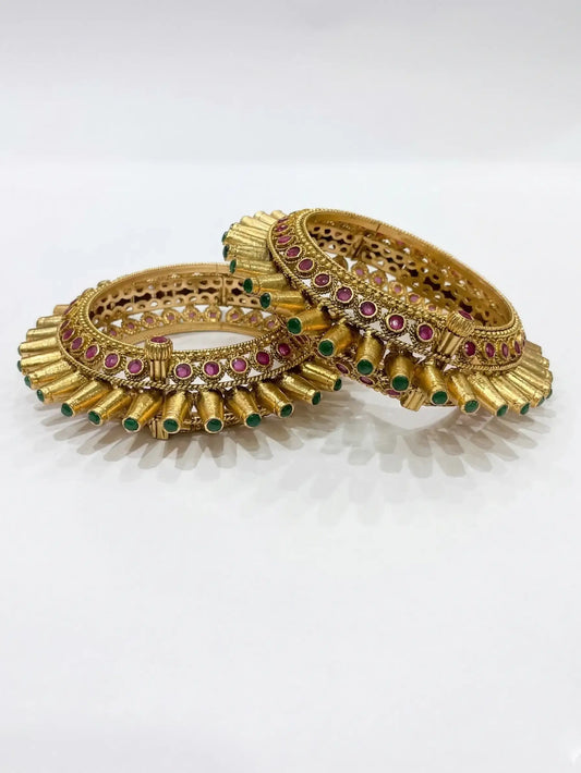 Pair of gold bangles with gemstones on a white background