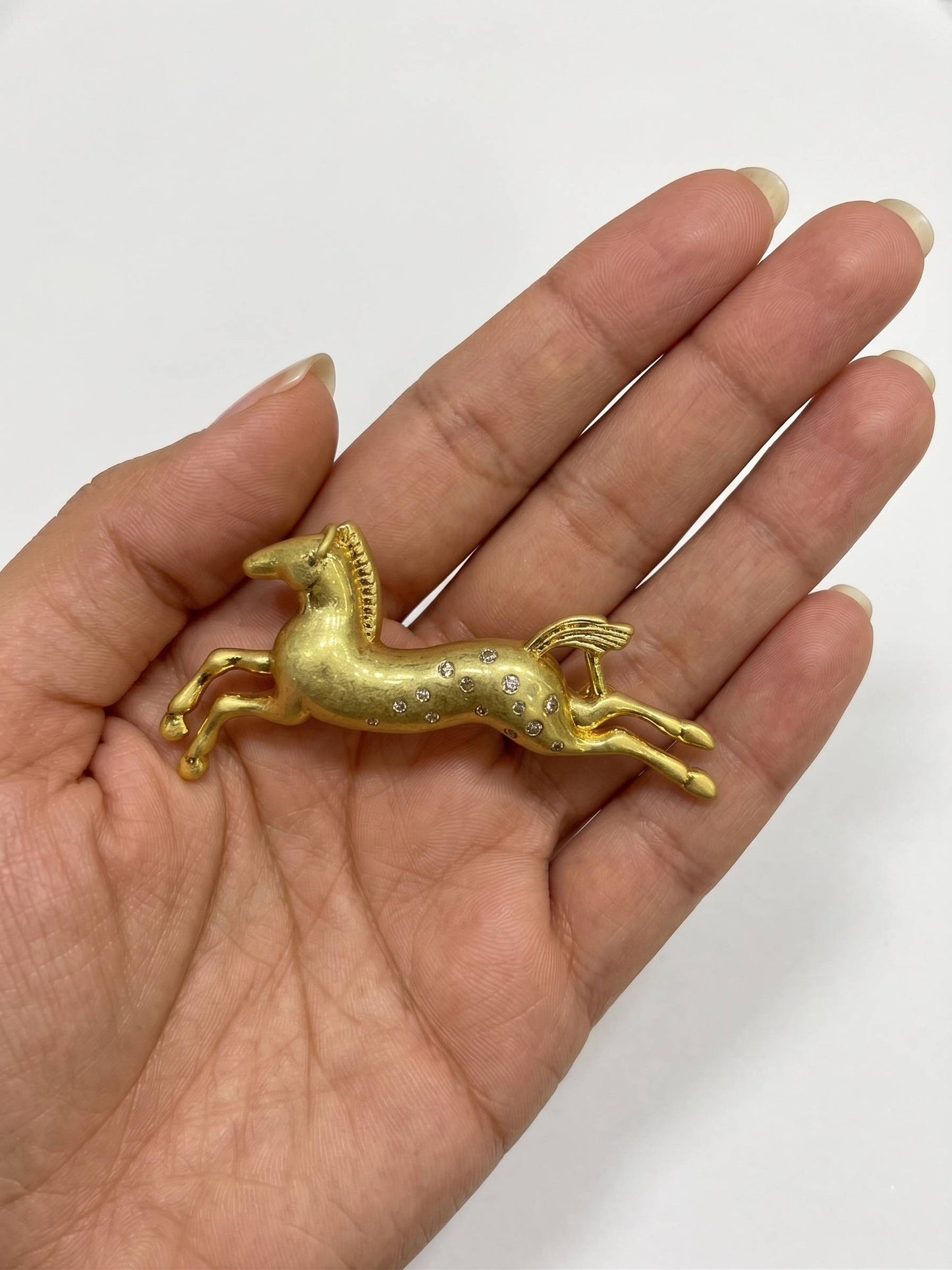 Gold horse-shaped brooch with embedded stones on a white background