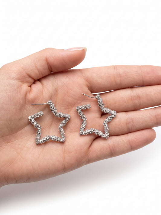 Star-shaped silver earrings held in a hand on a white background