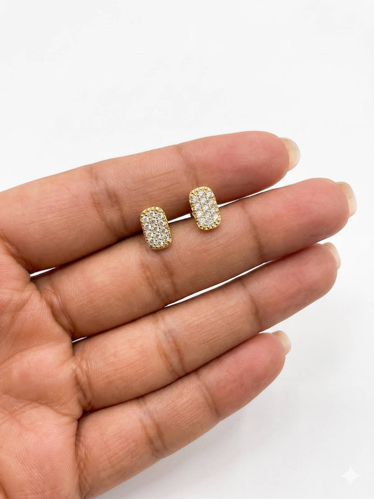 Gold earrings with clear stones held between fingers on a white background