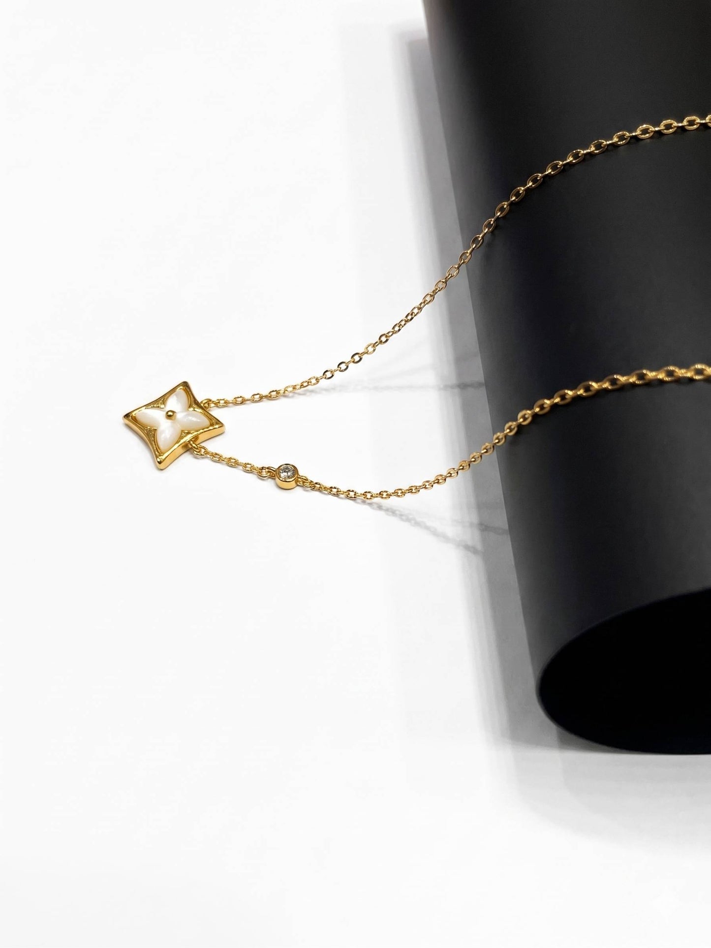 Gold star-shaped pendant on a chain against a black cylindrical object.