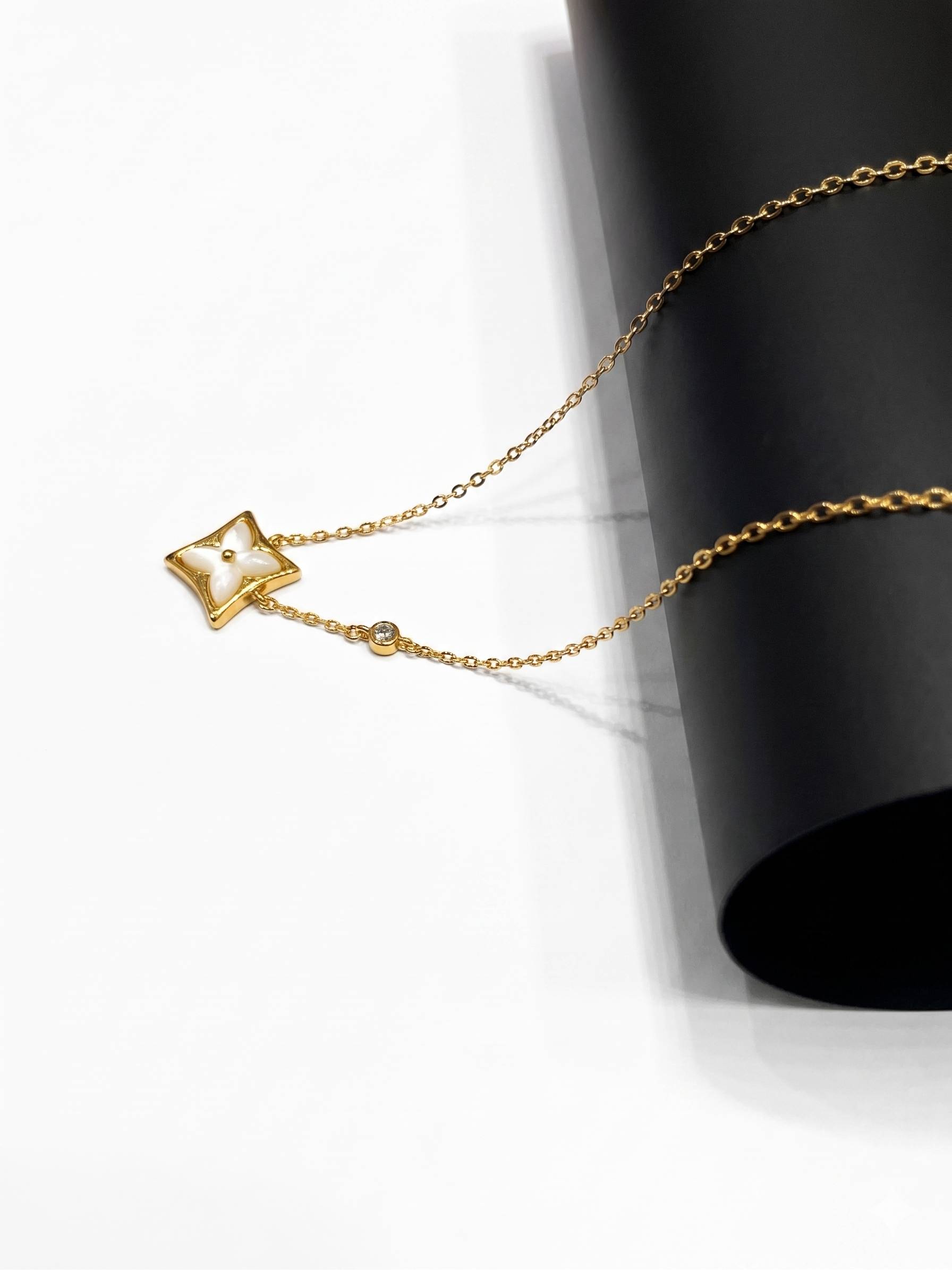 Gold star-shaped pendant on a chain against a black cylindrical object.