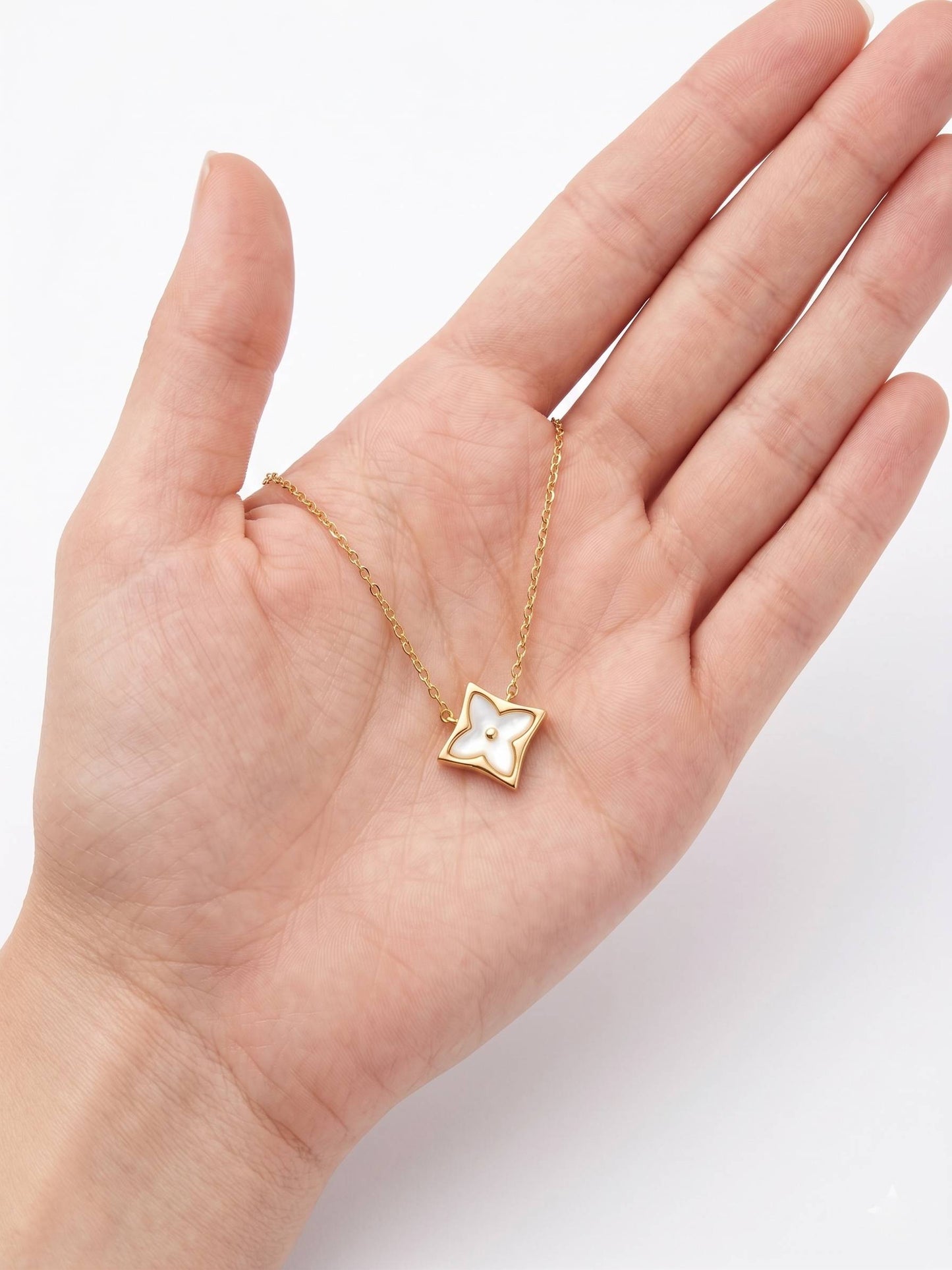 Gold necklace with a star-shaped pendant on a hand against a white background