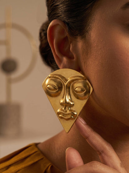 Gold face-shaped earring worn by a person with a blurred background