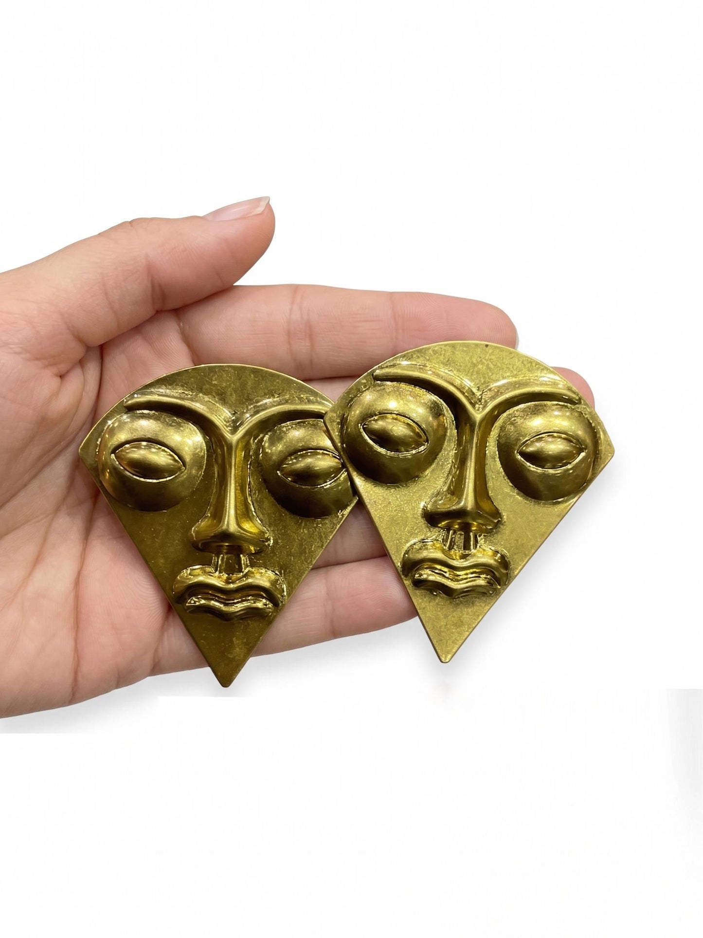Gold face-shaped earrings held in a hand against a white background
