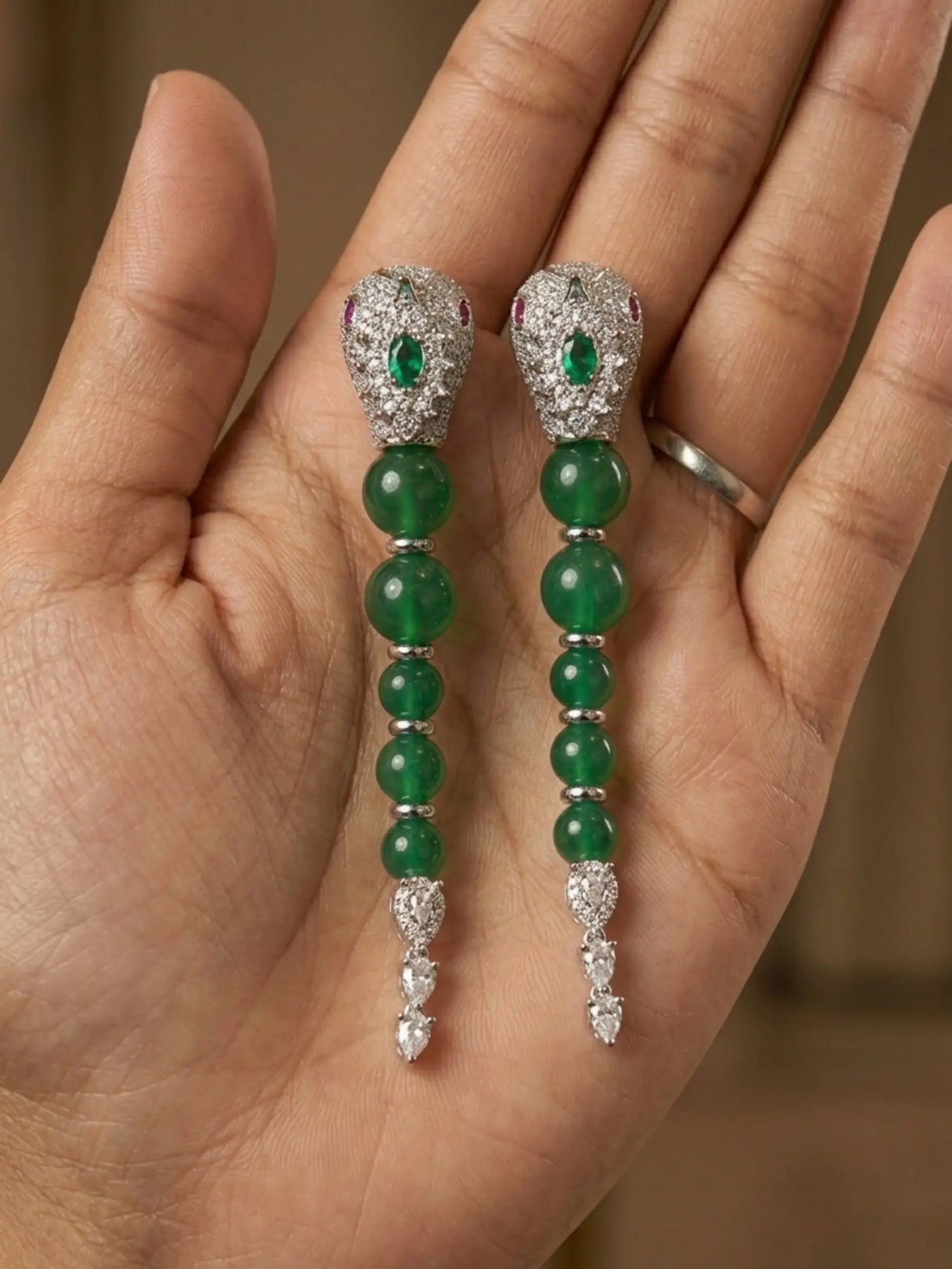 Green gemstone earrings with silver accents held in a hand against a neutral background