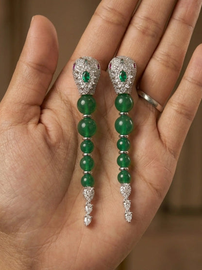 Green gemstone earrings with silver accents held in a hand against a neutral background