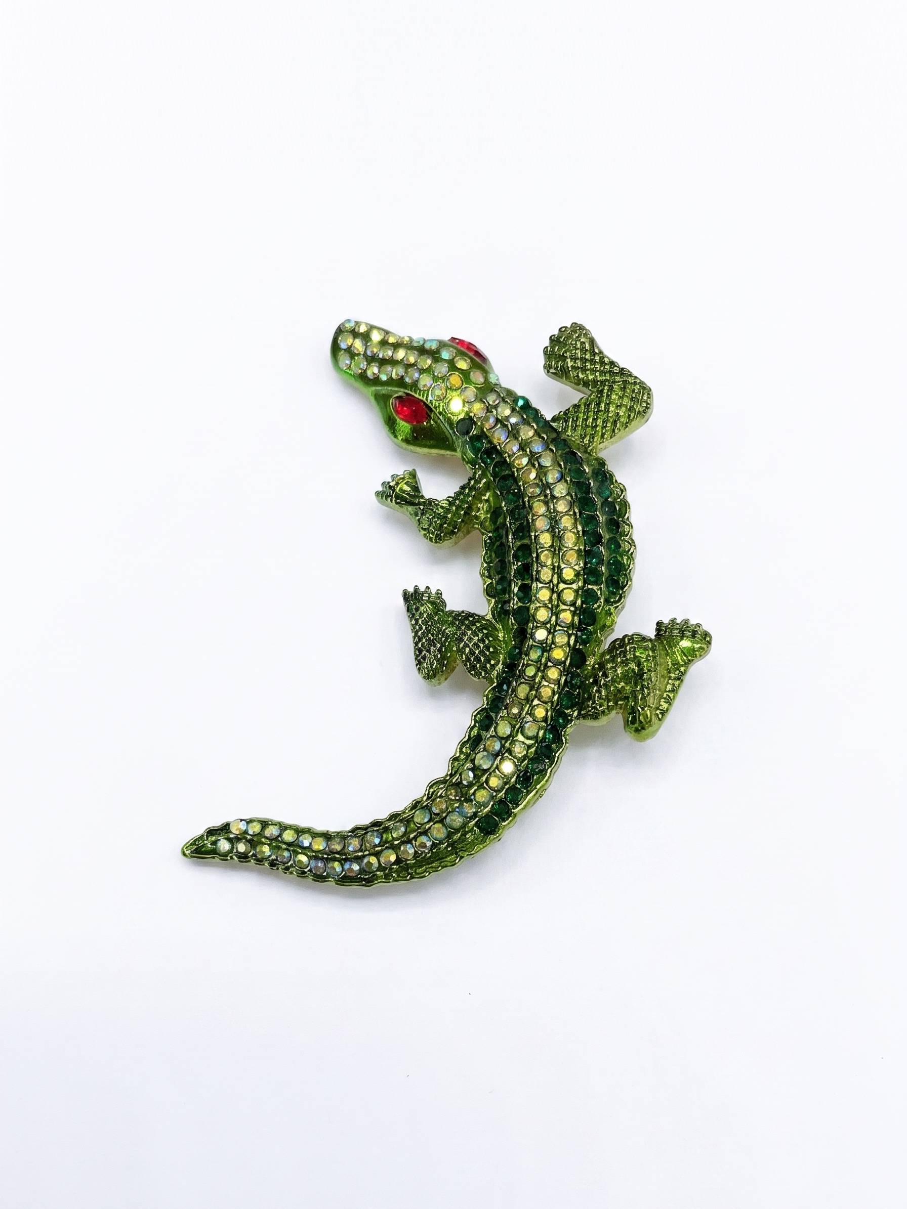 Green alligator-shaped brooch with red eyes on a white background