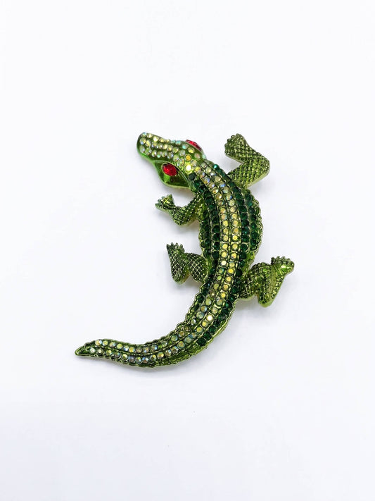 Green alligator-shaped brooch with red eyes on a white background