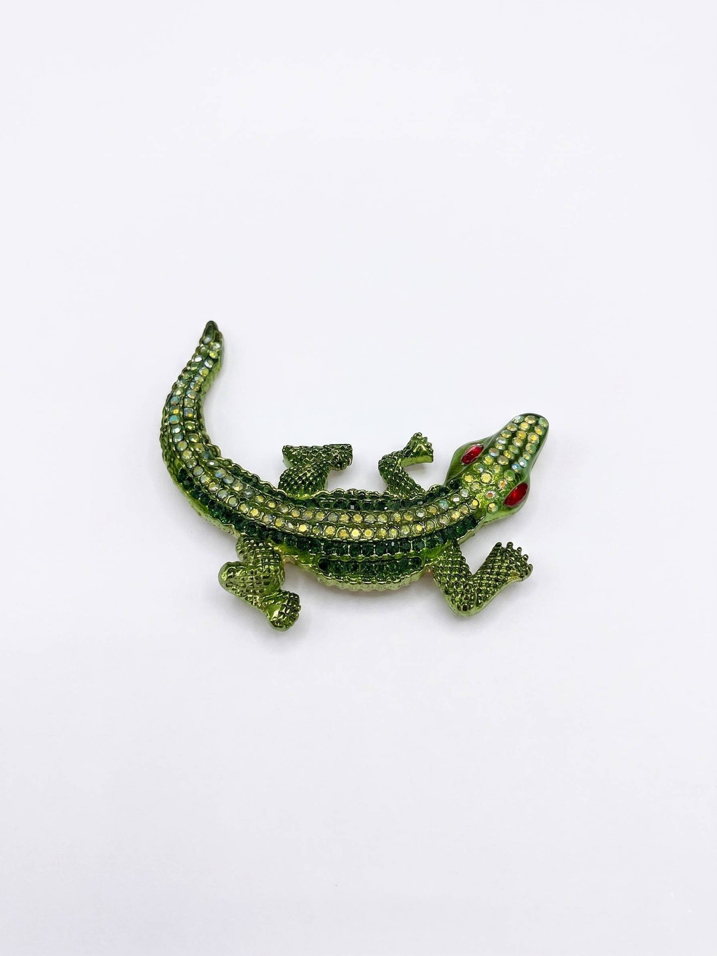 Green lizard-shaped brooch with red eyes on a white background