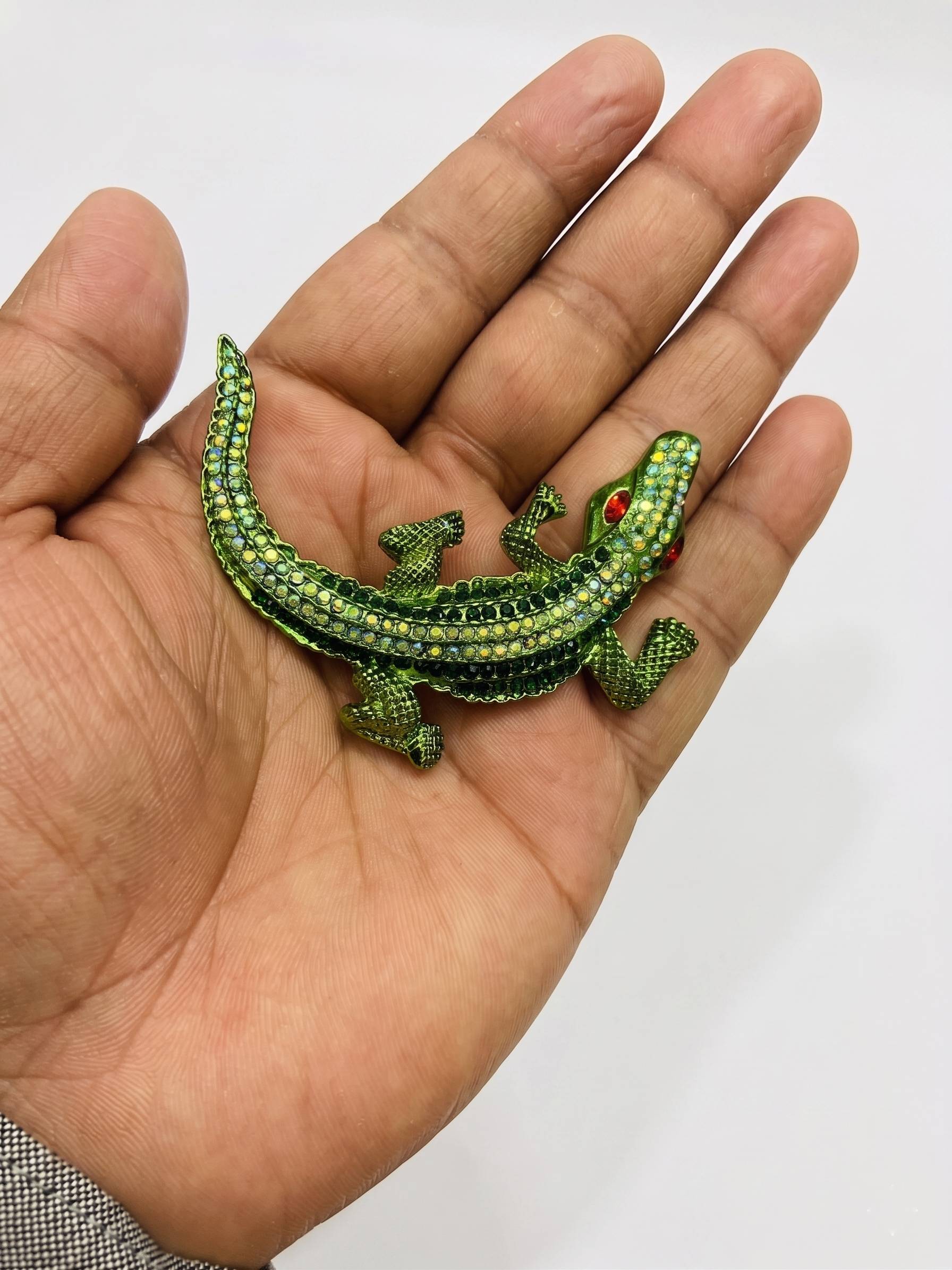 Green crocodile-shaped jewelry on a hand against a white background