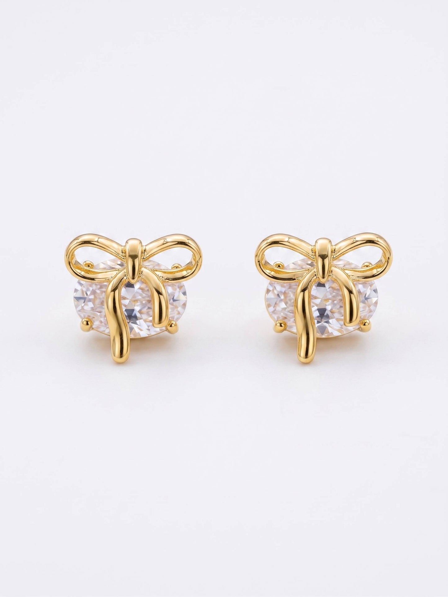 Gold bow-shaped earrings with clear gemstones on a white background