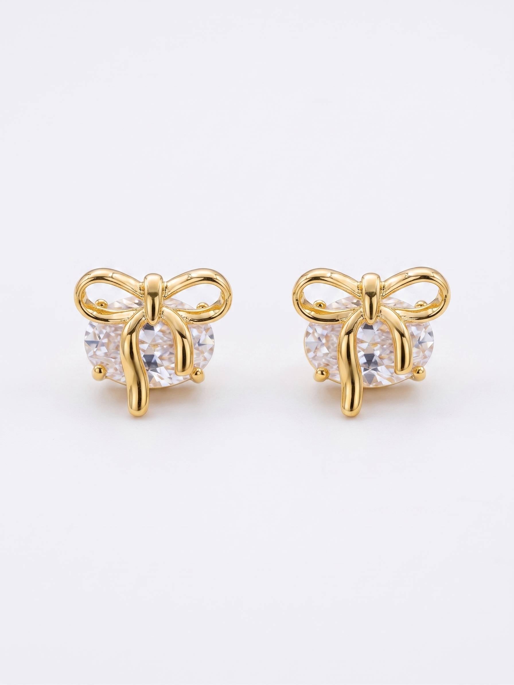 Gold bow-shaped earrings with clear gemstones on a white background