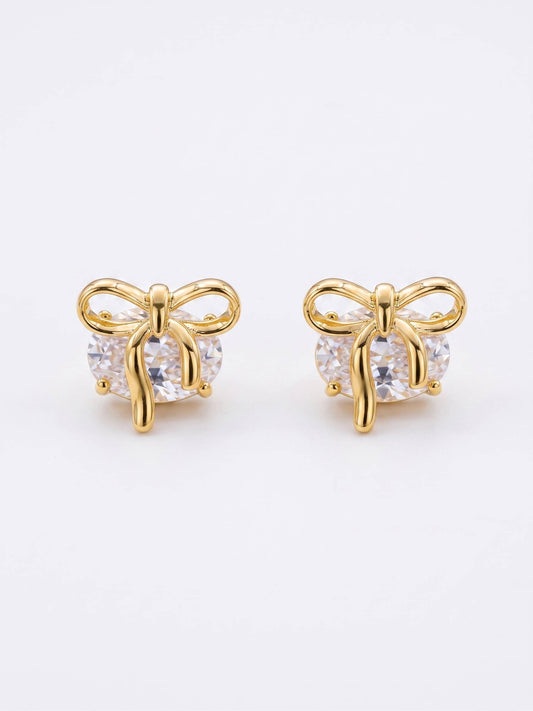 Gold bow-shaped earrings with clear gemstones on a white background
