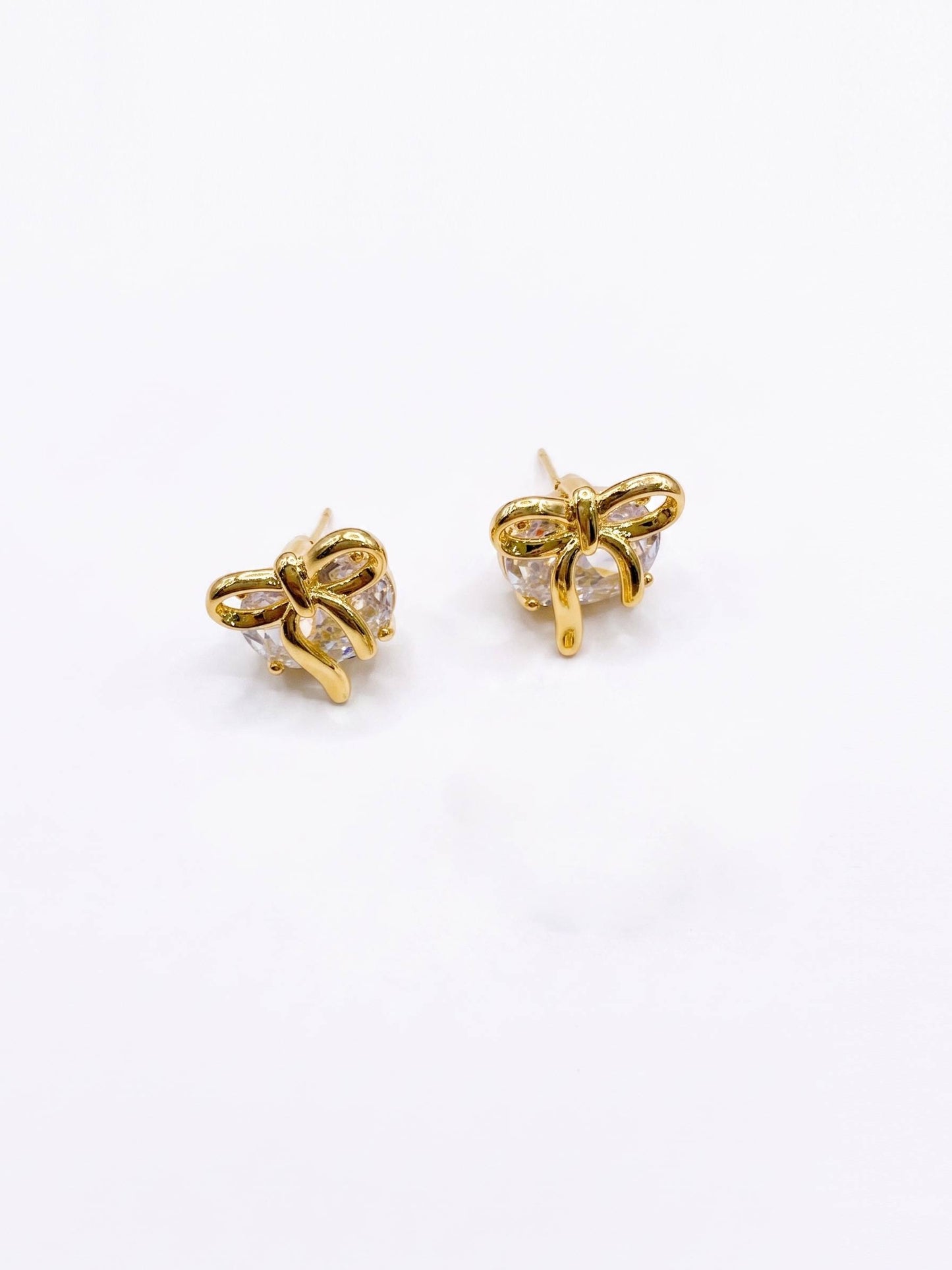 Gold bow-shaped earrings with clear gemstones on a white background