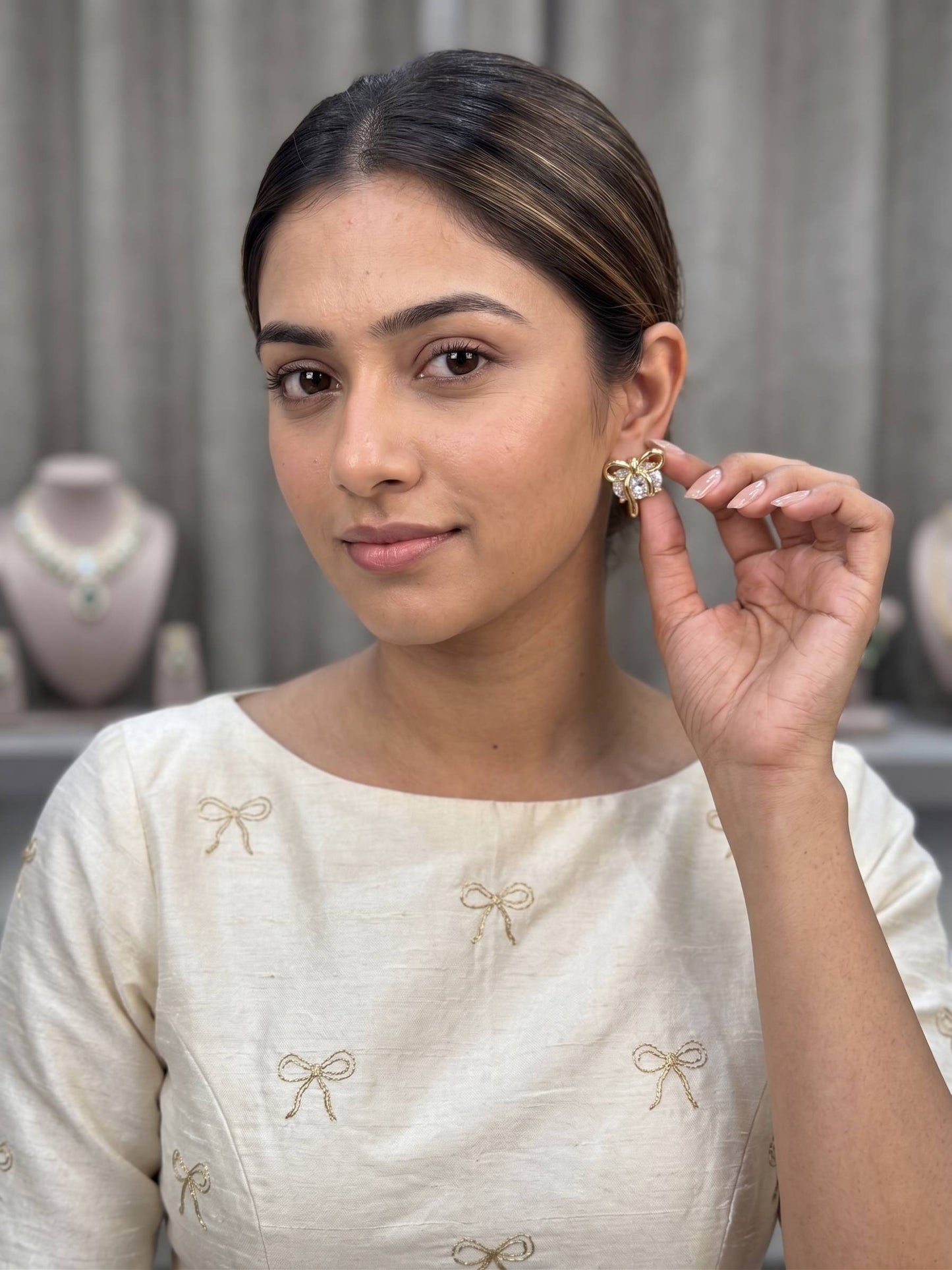 Woman wearing a white blouse with gold embroidery, holding an earring.