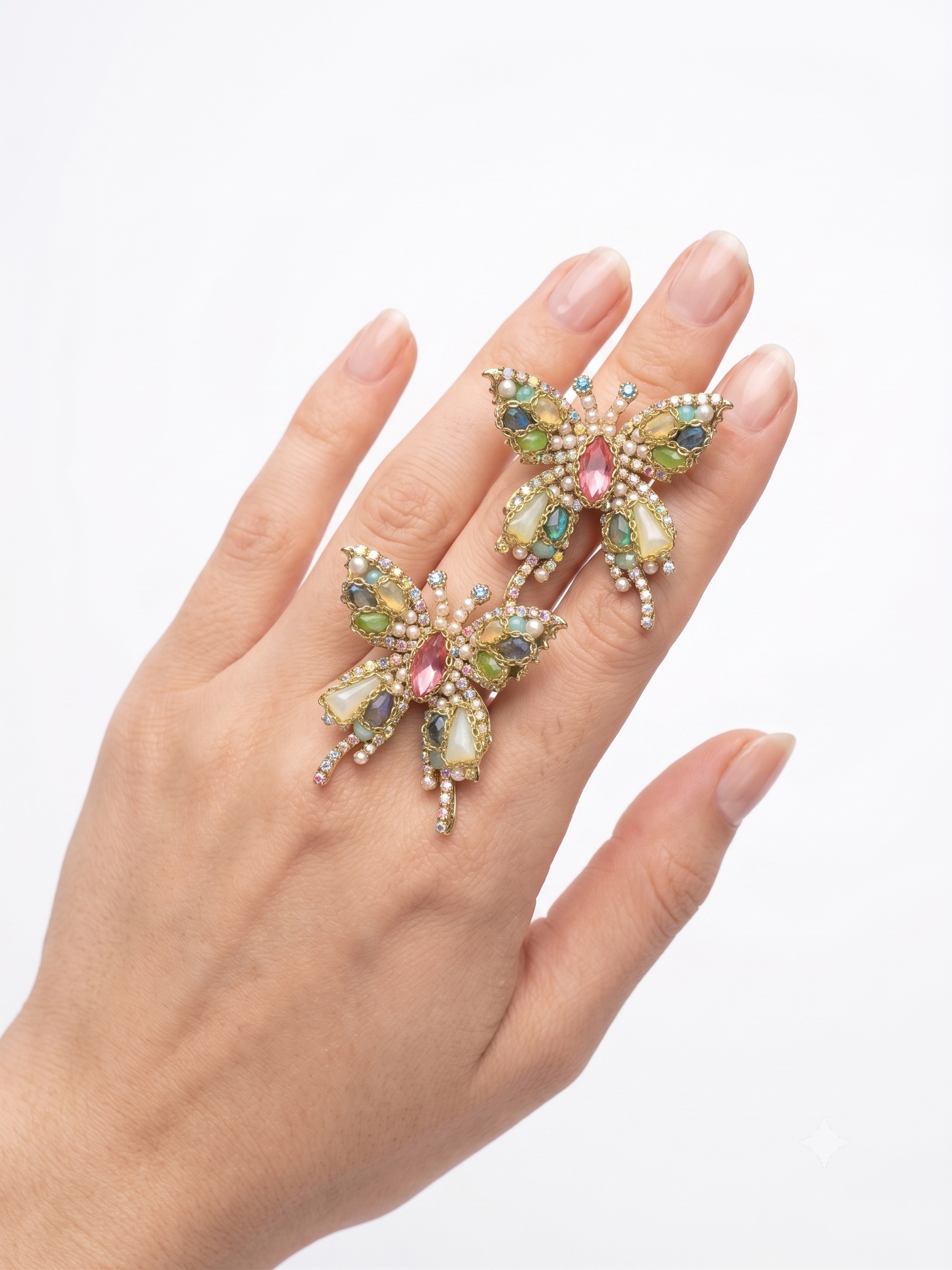 Hand wearing a decorative ring with colorful gemstones on a white background
