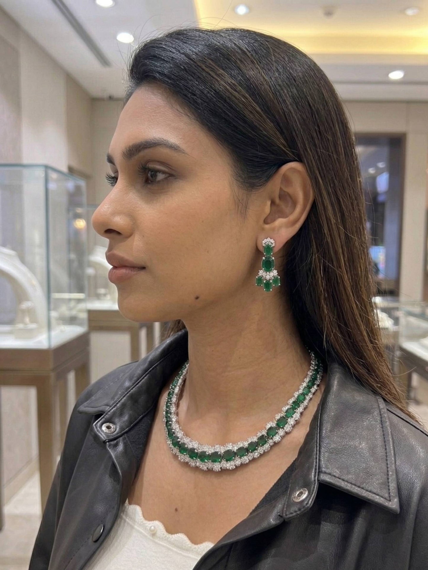Woman wearing a green and white emerald necklace and earrings in a jewelry store.