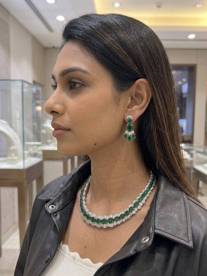 Woman wearing a green and white emerald necklace and earrings in a jewelry store.