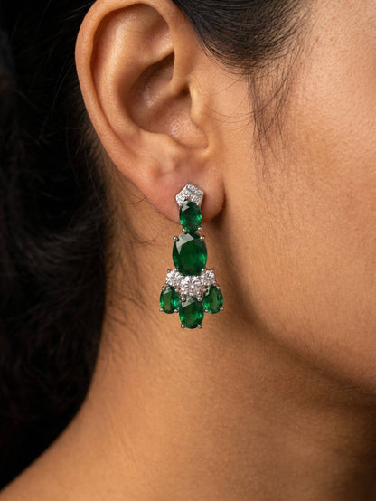 Close-up of a person wearing emerald green earrings with clear stones.