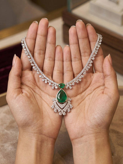 Silver necklace with a green gemstone held between two hands against a blurred background