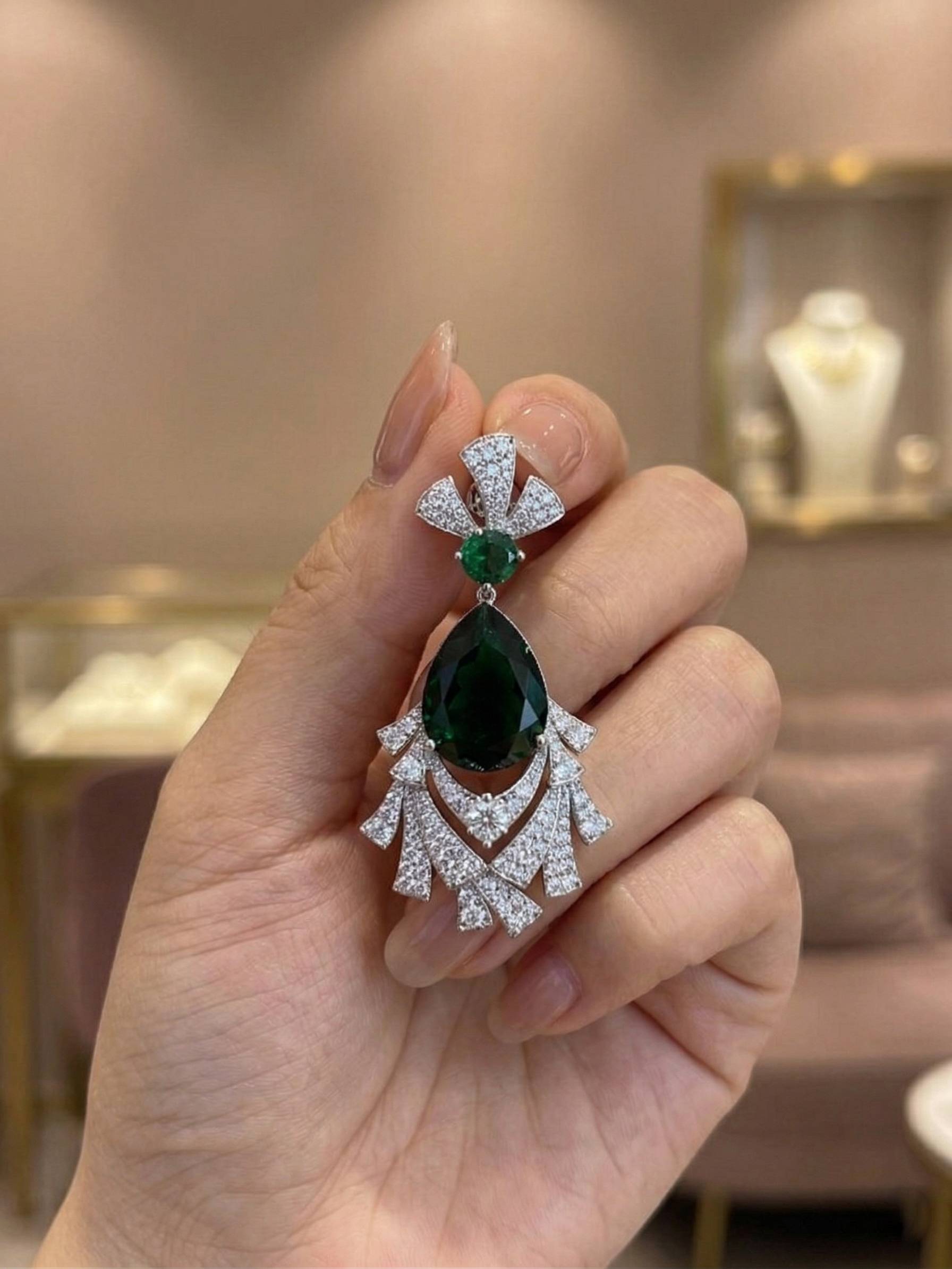 Hand holding a diamond and emerald earring with a blurred jewelry store background