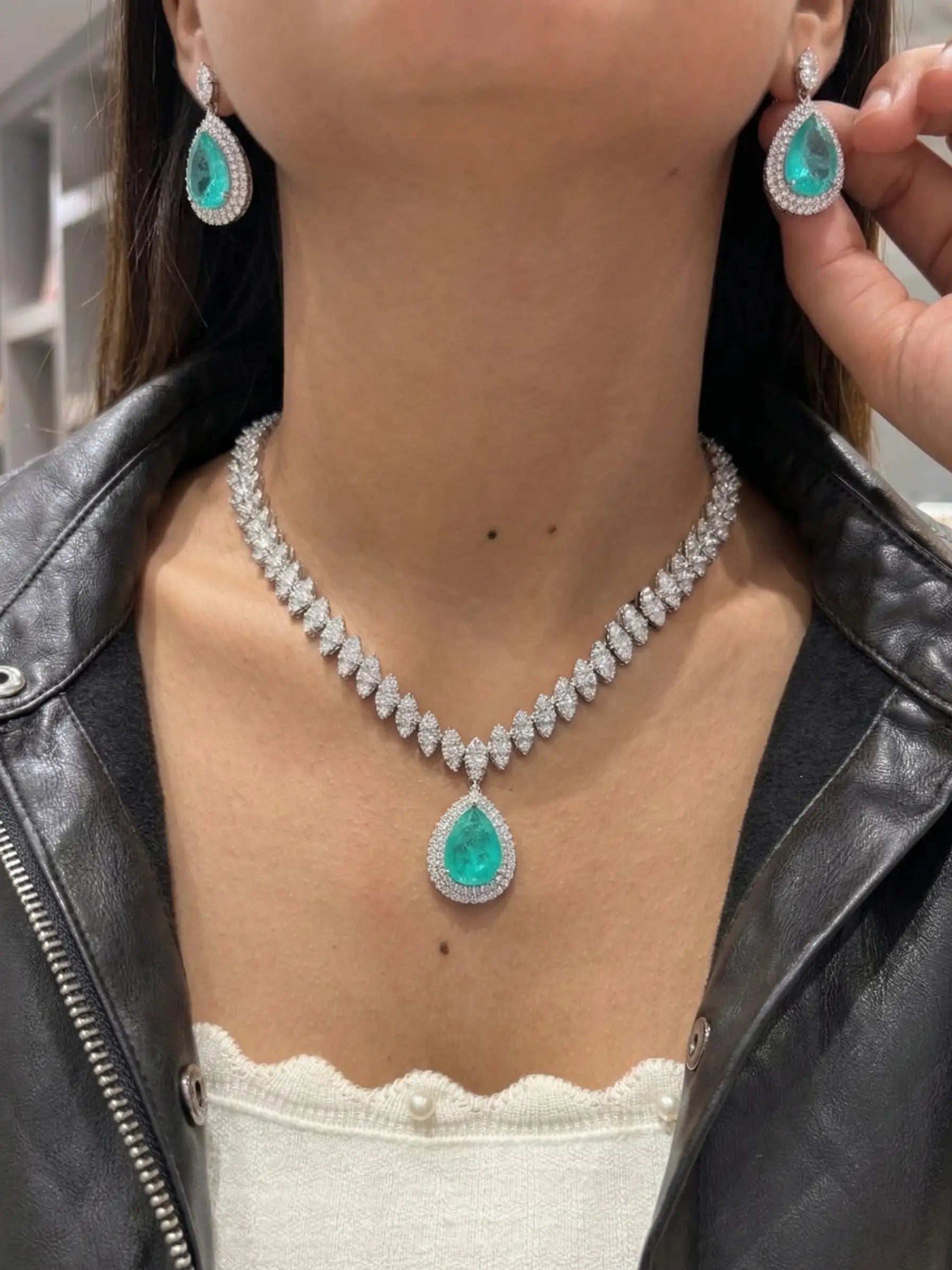 Person wearing a diamond necklace with emerald green pendants and matching earrings.