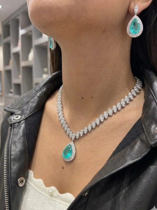 Person wearing a diamond necklace and earrings with emerald green gemstones.