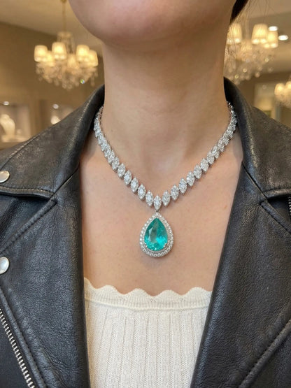 Person wearing a necklace with a green gemstone in a blurred indoor setting