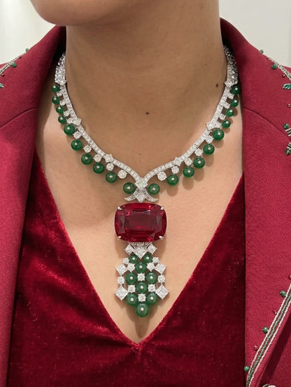 Luxury jewelry necklace with red gemstone and green beads worn by a person in a red outfit.