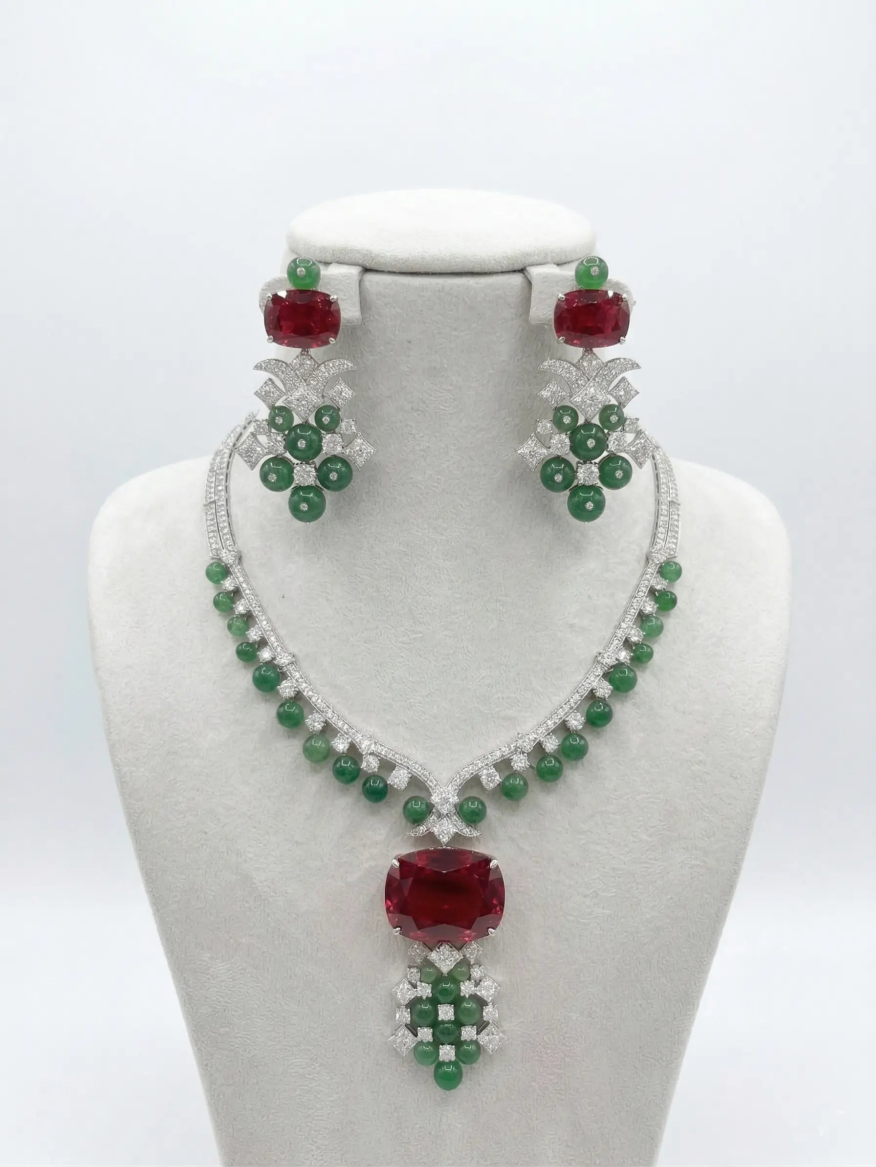 Jewelry set with necklace and earrings featuring red and green stones on a white background