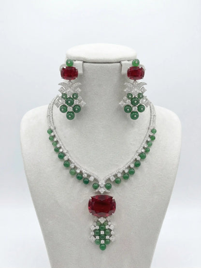 Jewelry set with necklace and earrings featuring red and green stones on a white background