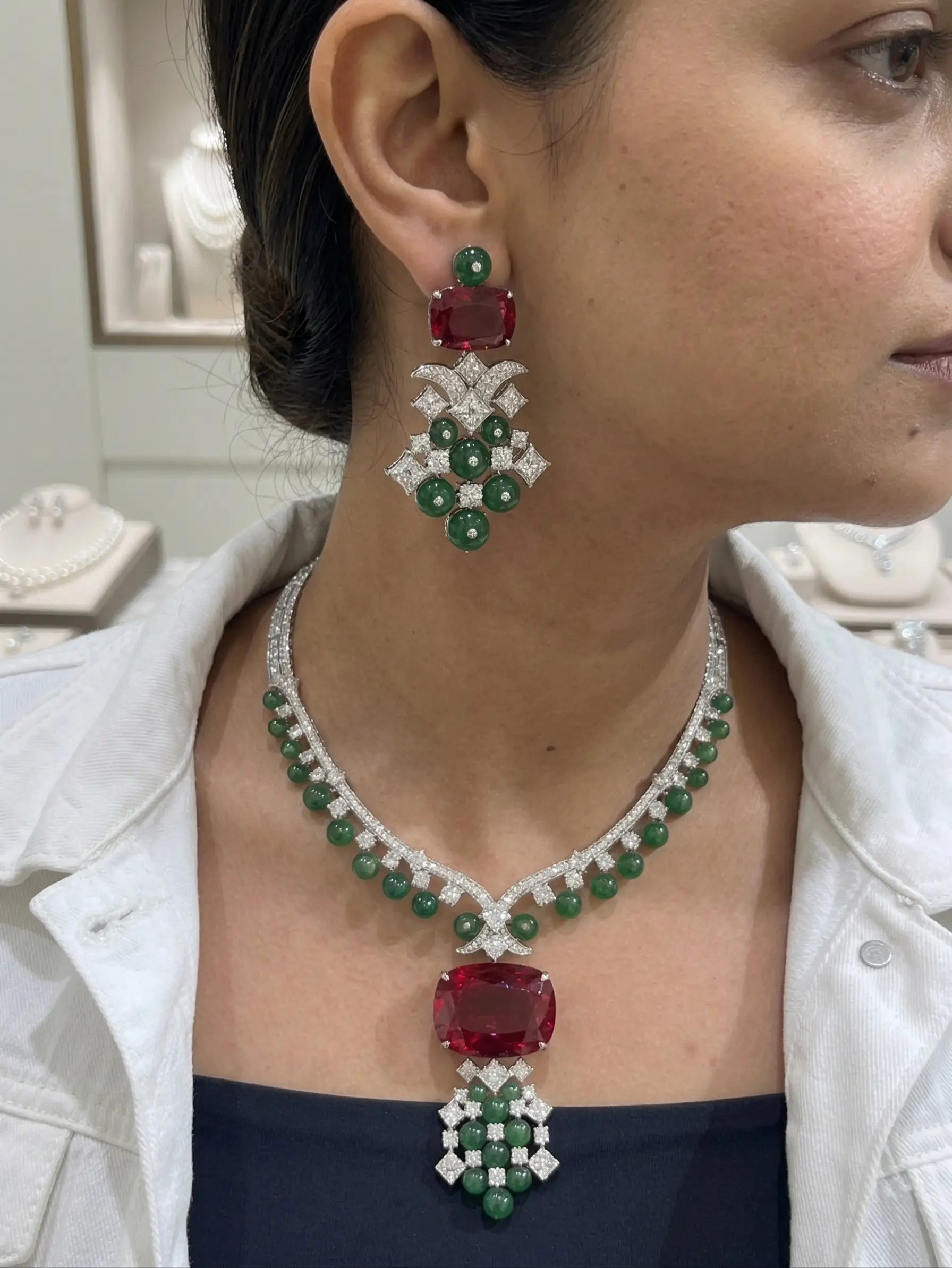 Woman wearing a luxurious emerald and red gemstone necklace and earrings.