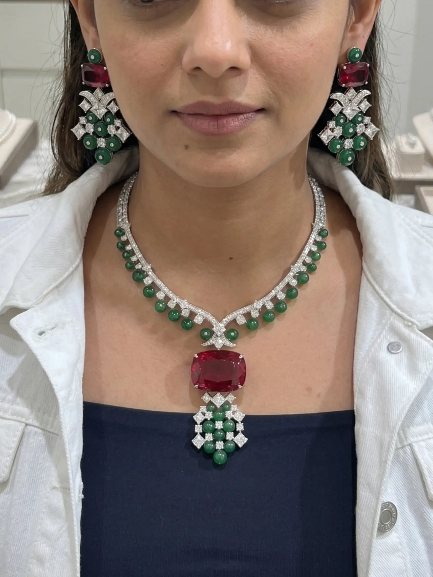 Woman wearing a luxurious emerald and ruby necklace with matching earrings.
