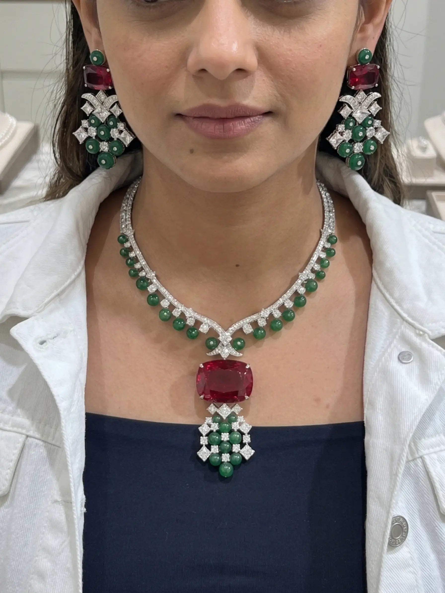 Woman wearing a luxurious emerald and ruby necklace with matching earrings.