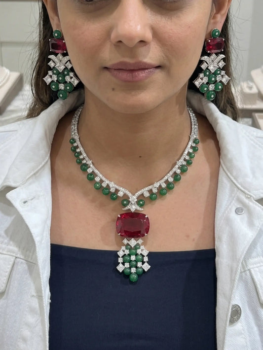 Woman wearing a luxurious emerald and ruby necklace with matching earrings.