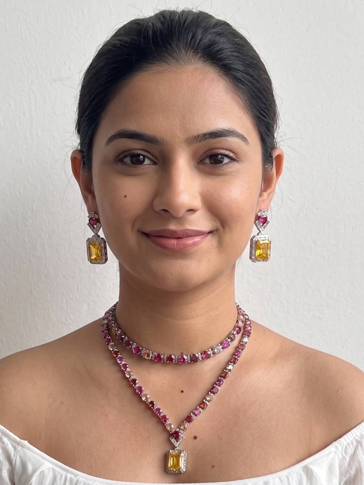 Woman wearing a necklace and earrings with gemstones on a plain background