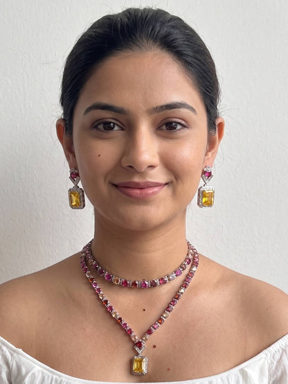 Woman wearing a necklace and earrings with gemstones on a plain background