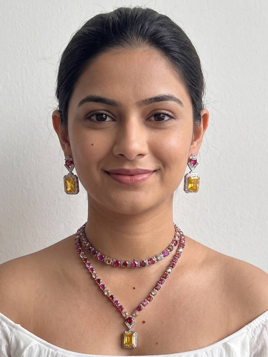 Woman wearing a necklace and earrings with gemstones on a plain background