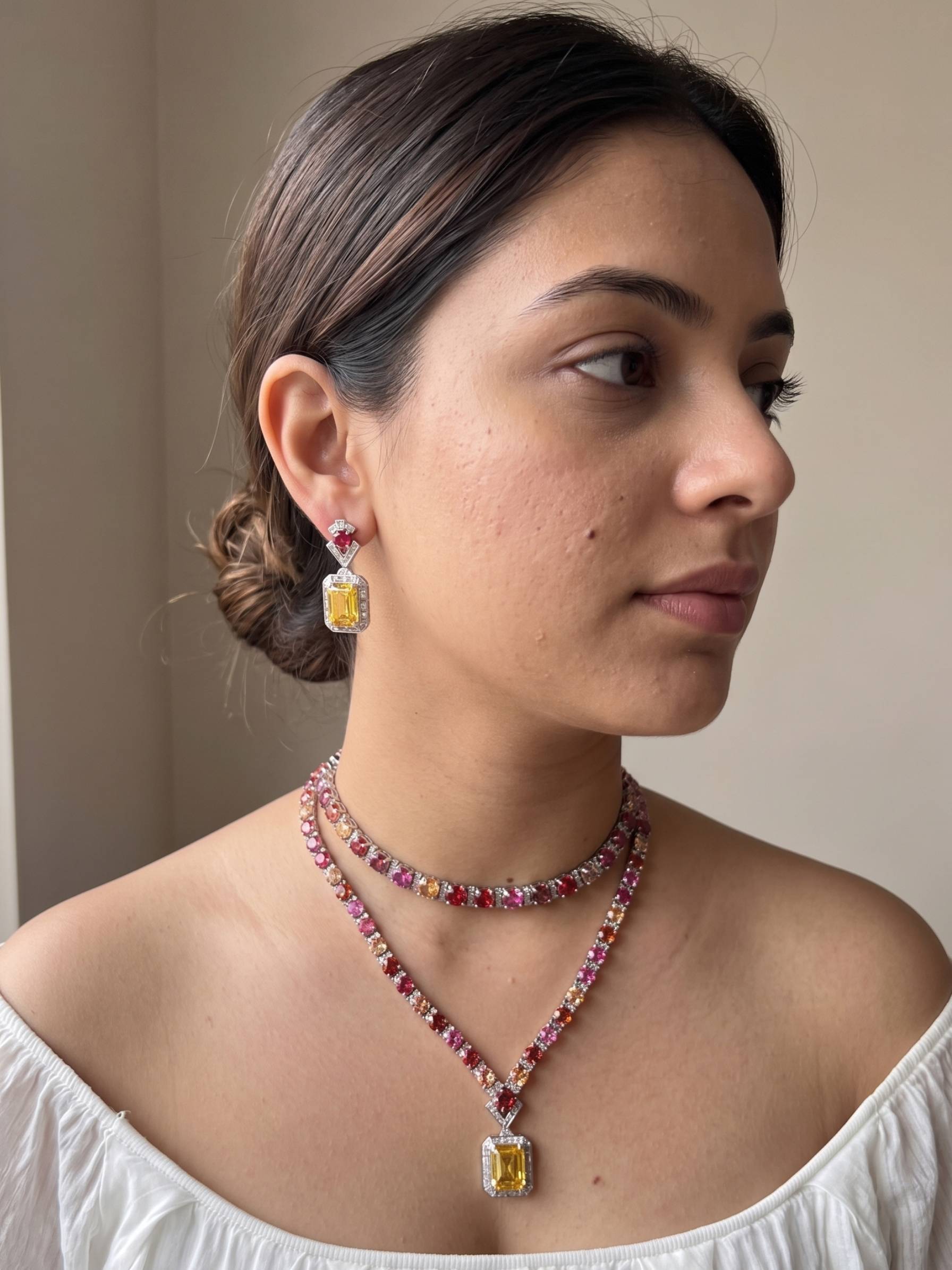 Woman wearing a necklace and earrings with yellow gemstones against a neutral background