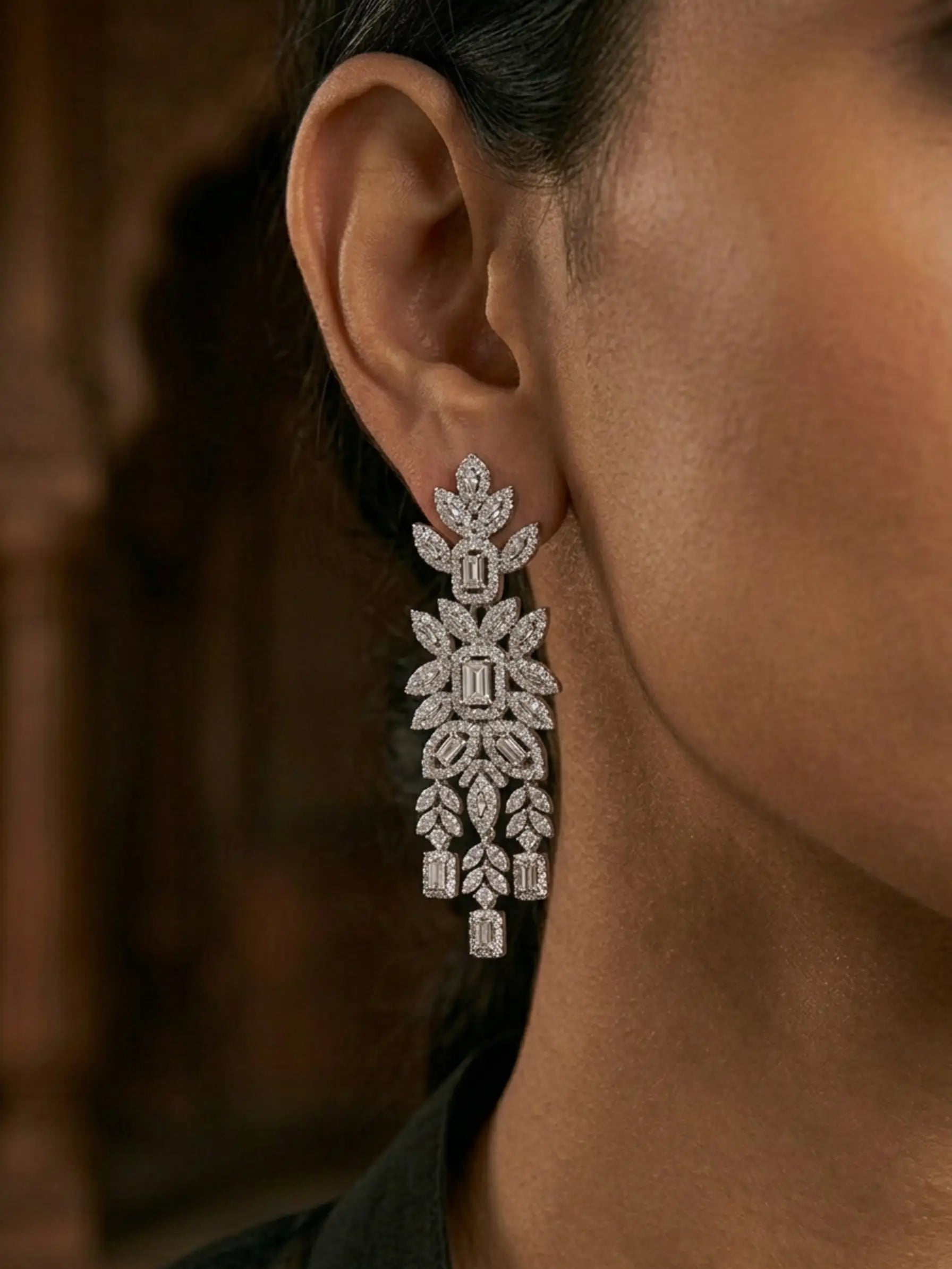 Close-up of a person wearing a sparkling diamond earring against a blurred background