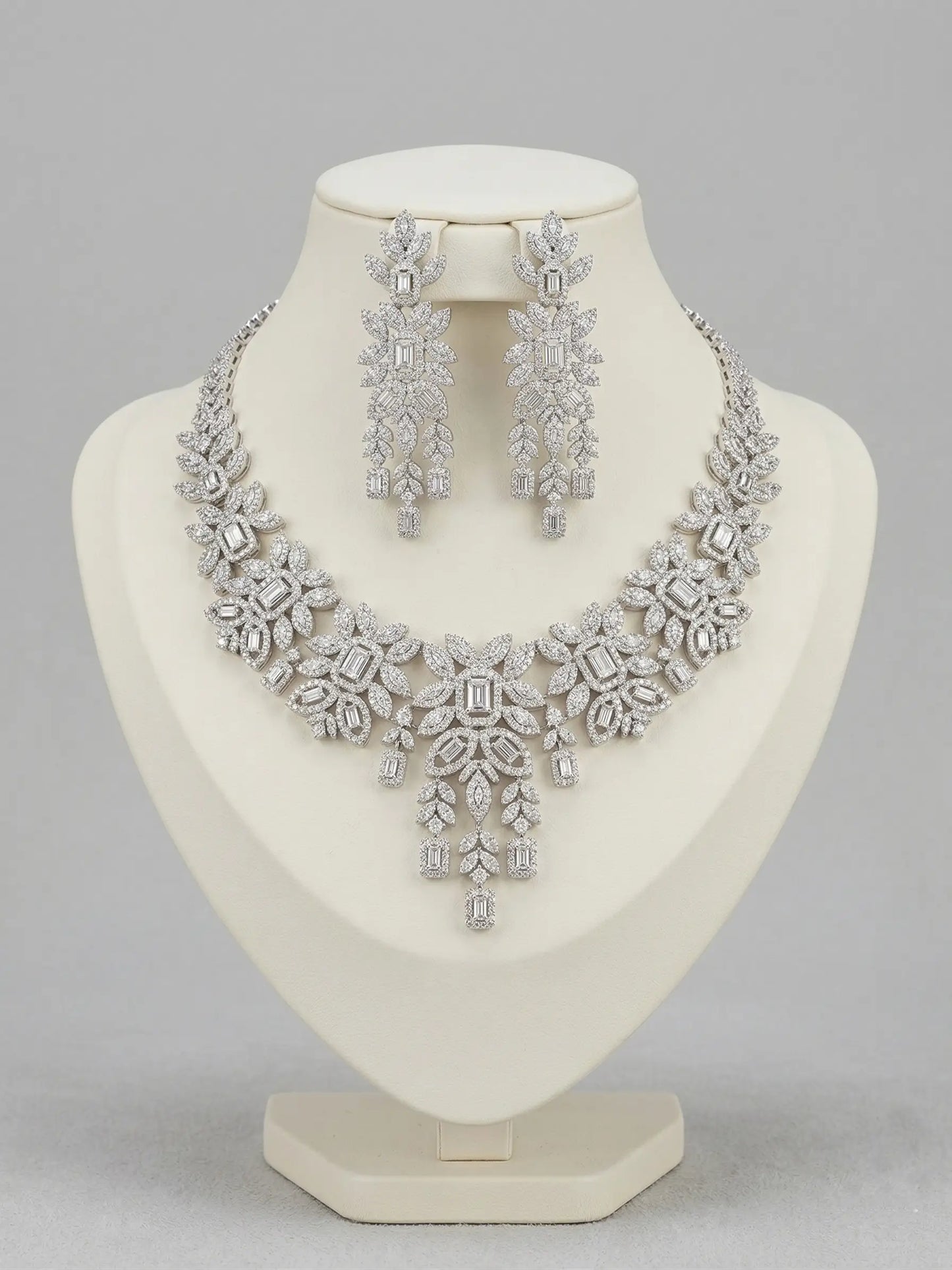 Silver necklace and earrings set on a mannequin bust against a gray background