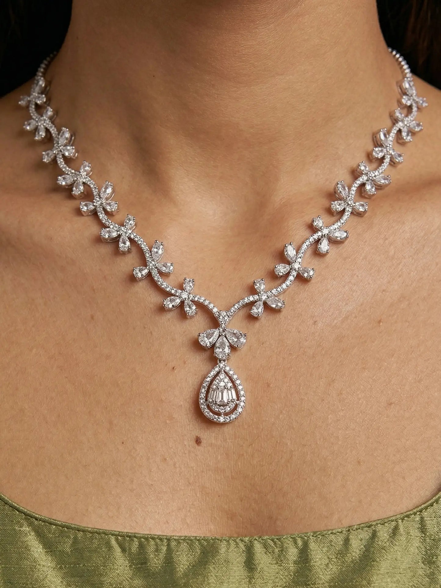 Silver necklace with floral design and teardrop pendant on a person wearing a green top.