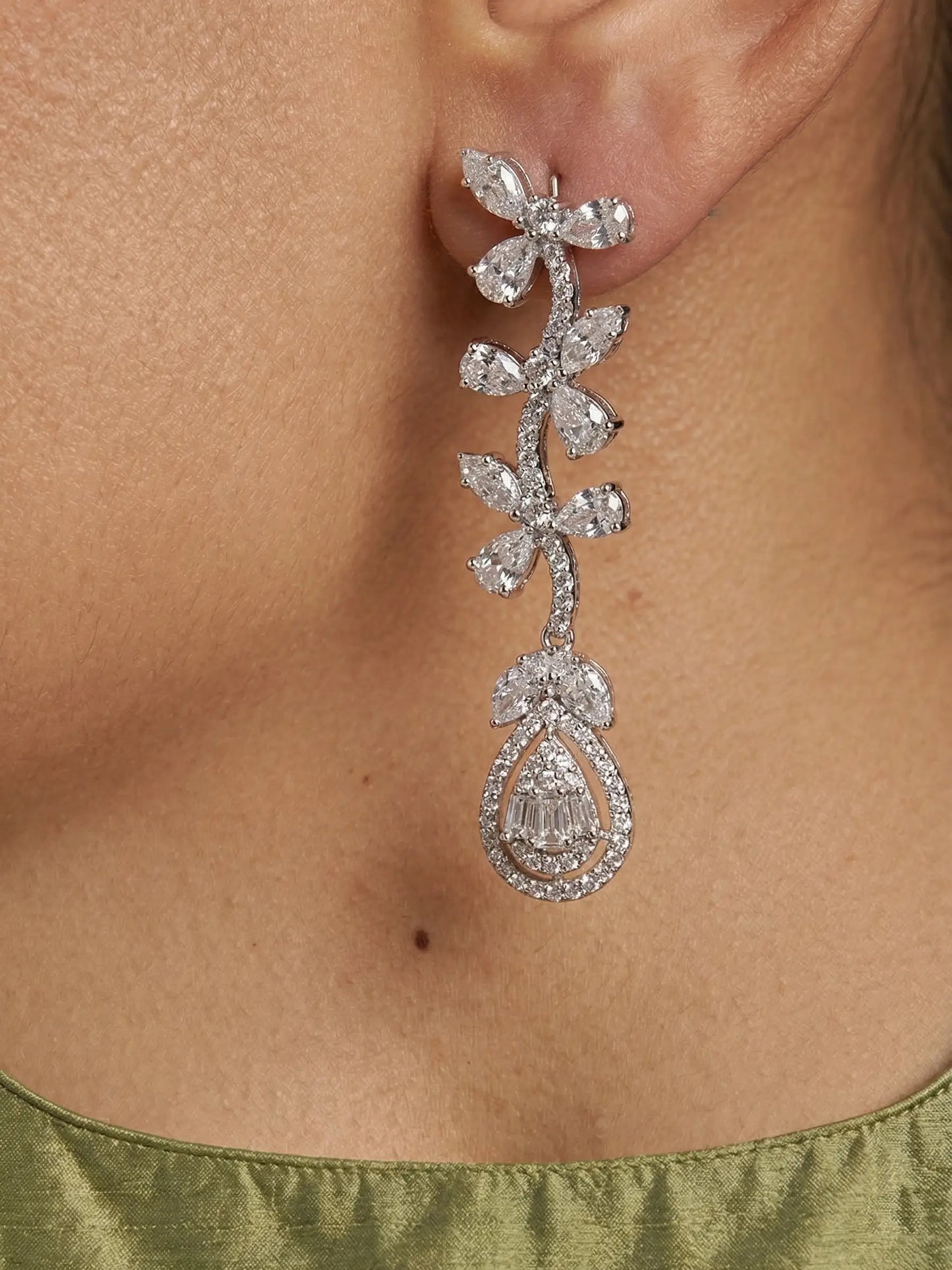 Close-up of a diamond earring on a person's ear with a green garment.