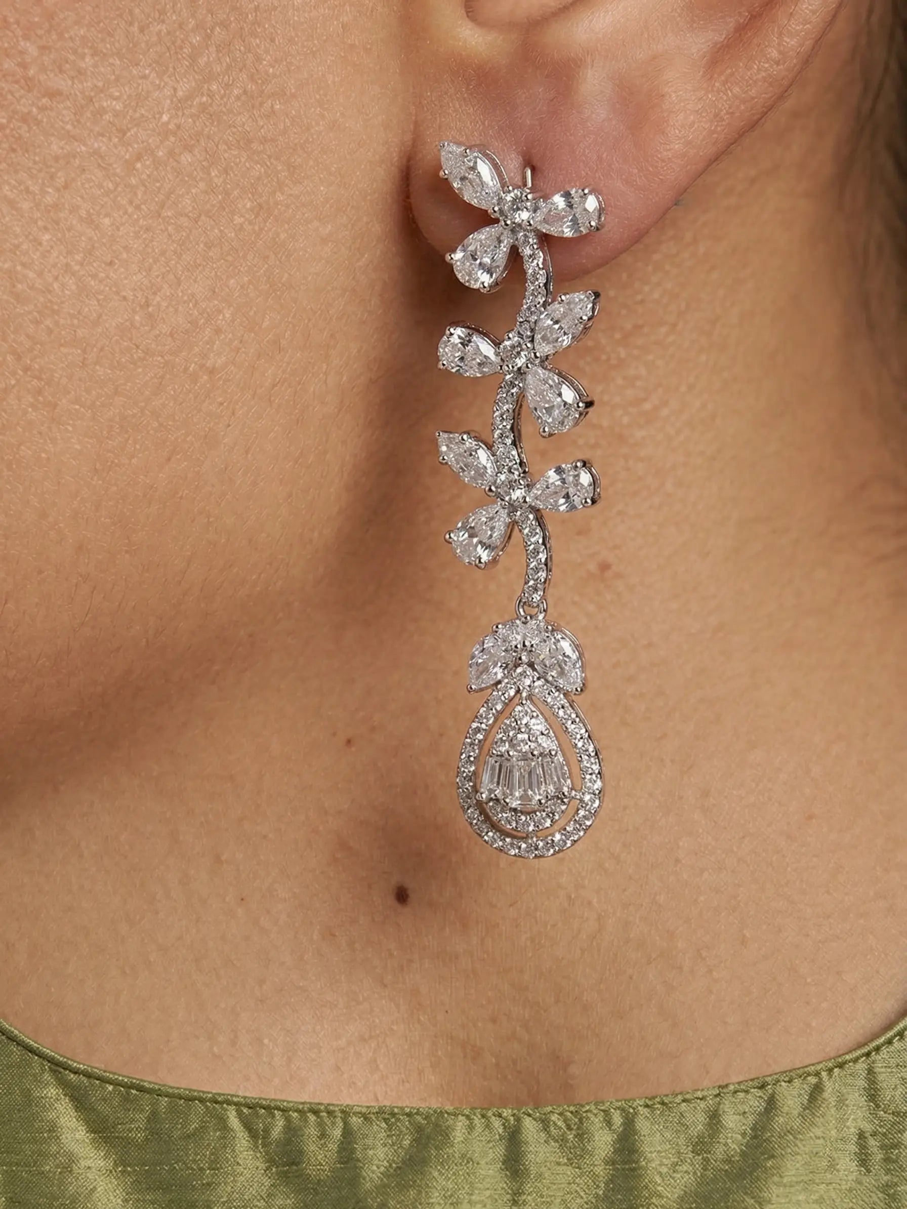 Close-up of a diamond earring on a person's ear with a green garment.
