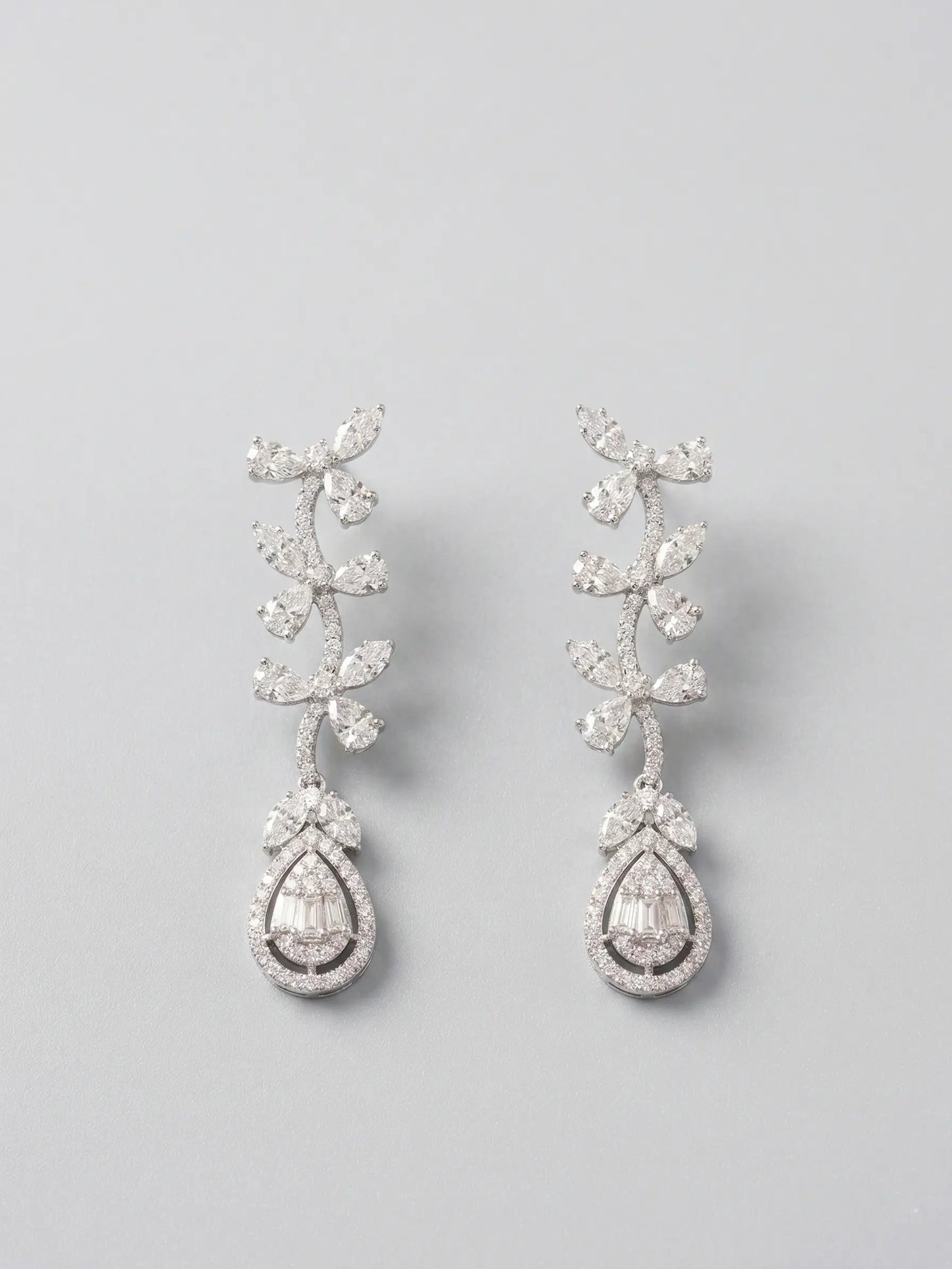 Pair of silver teardrop earrings with clear gemstones on a light gray background
