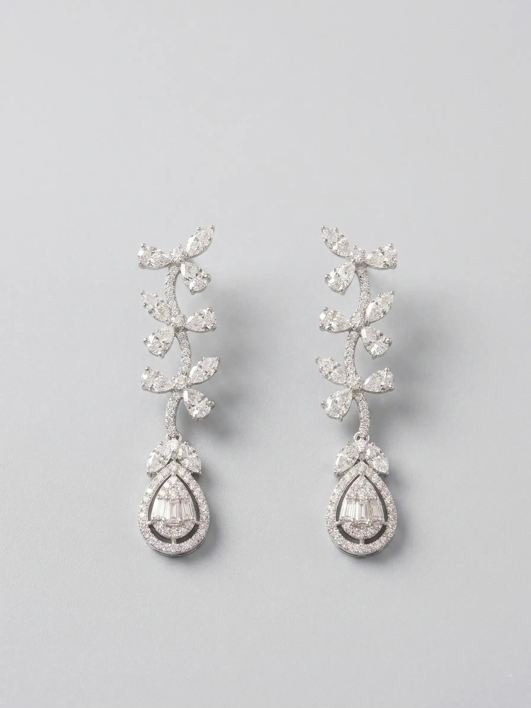 Pair of silver teardrop earrings with clear gemstones on a light gray background