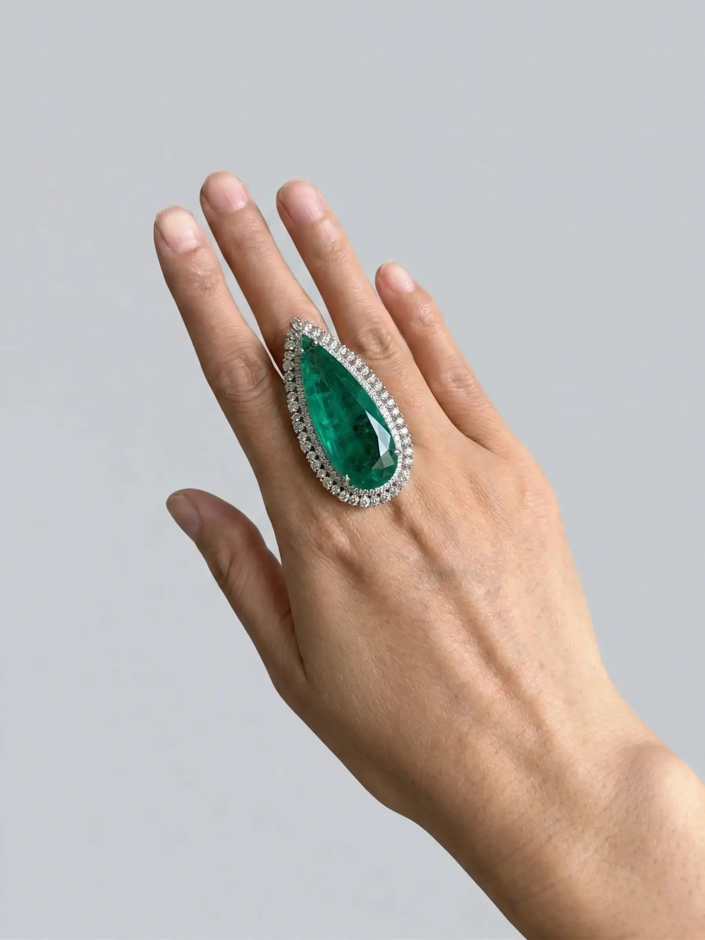 Hand wearing a ring with a large green gemstone on a gray background