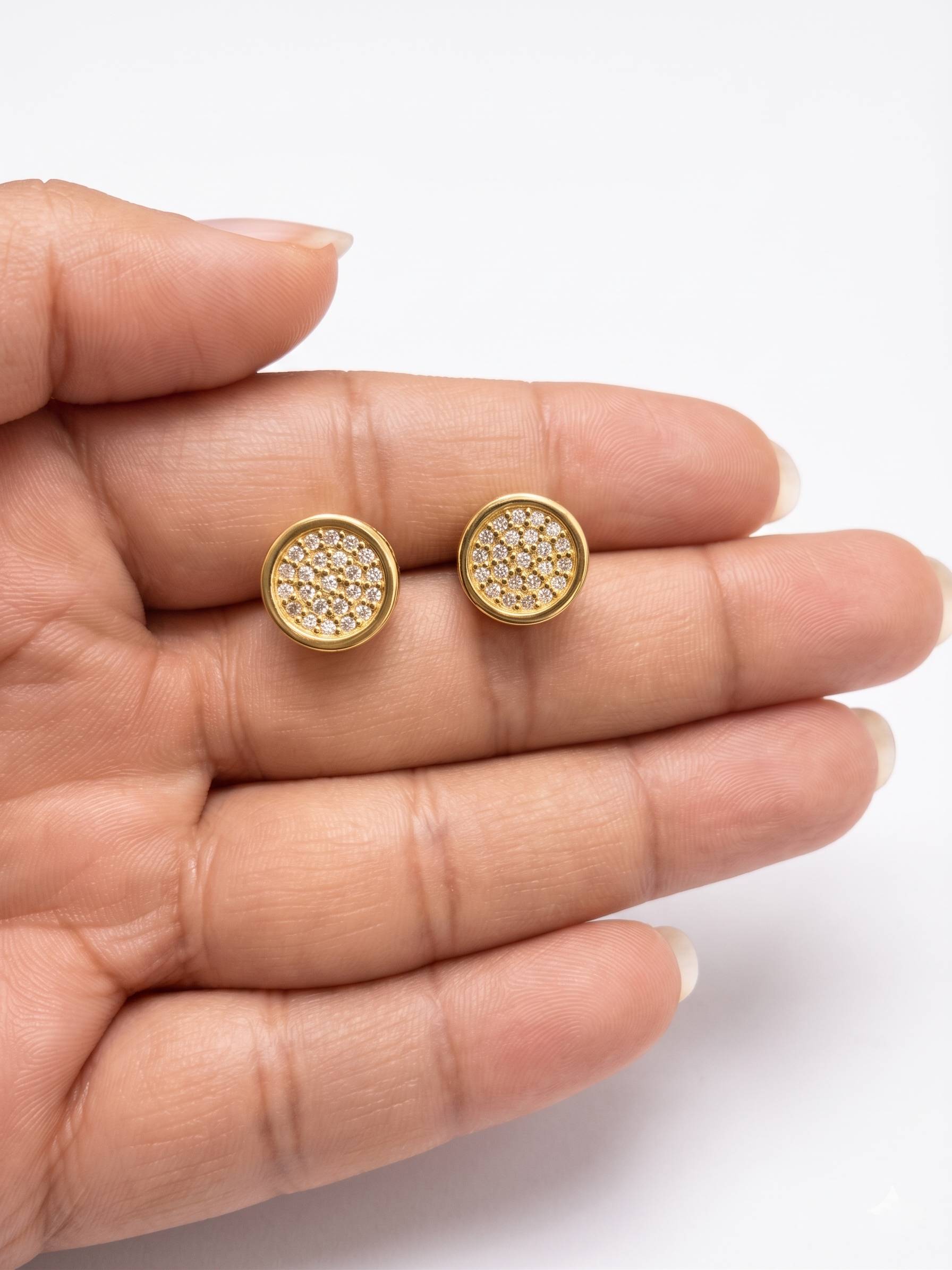 Gold stud earrings held between fingers on a white background